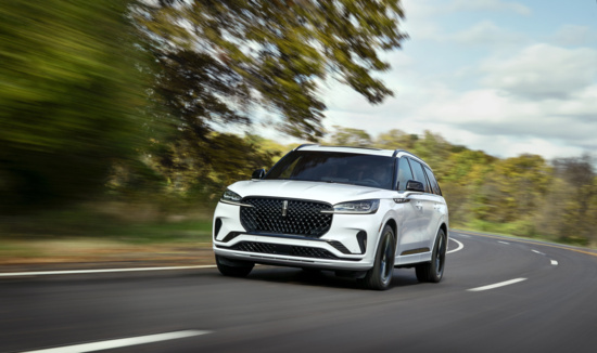 A sleek white SUV speeds along a curved road bordered by blurred green trees under a partly cloudy sky, conveying motion and freedom.