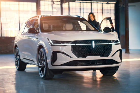 A white luxury SUV parked indoors with sunlight streaming through windows. A person stands by the open driver's door, conveying a modern and sophisticated feel.