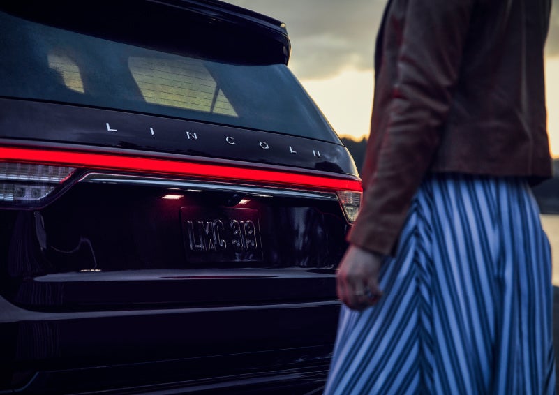 A person is shown near the rear of a 2024 Lincoln Aviator® SUV as the Lincoln Embrace illuminates the rear lights | Korum Lincoln in Puyallup WA