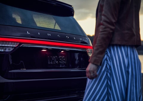 A person is shown near the rear of a 2024 Lincoln Aviator® SUV as the Lincoln Embrace illuminates the rear lights | Korum Lincoln in Puyallup WA