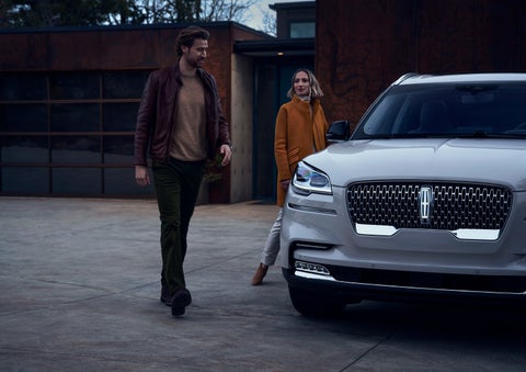 A man and a woman approaching a 2024 Lincoln Aviator® SUV, which illuminates certain lights when they are close | Korum Lincoln in Puyallup WA