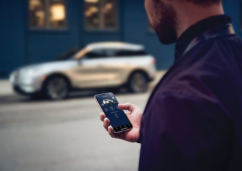A person is shown interacting with a smartphone to connect to a Lincoln vehicle across the street. | Korum Lincoln in Puyallup WA