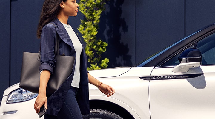 A woman approaches a 2024 Lincoln Corsair® SUV while holding a smartphone. | Korum Lincoln in Puyallup WA