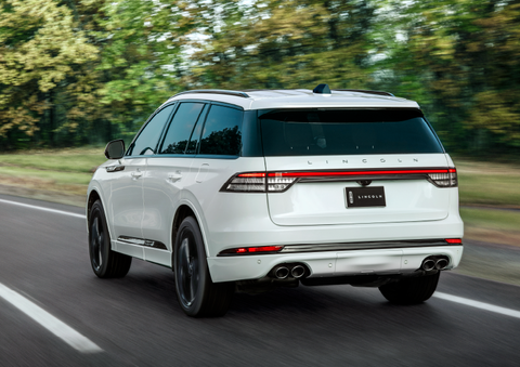A white 2025 Lincoln Aviator® SUV is being driven away down a road lined with colorful trees. | Korum Lincoln in Puyallup WA