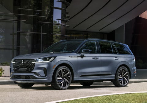A gray 2025 Lincoln Aviator® SUV is parked outside a modern building showcasing the driver’s side of the vehicle. | Korum Lincoln in Puyallup WA