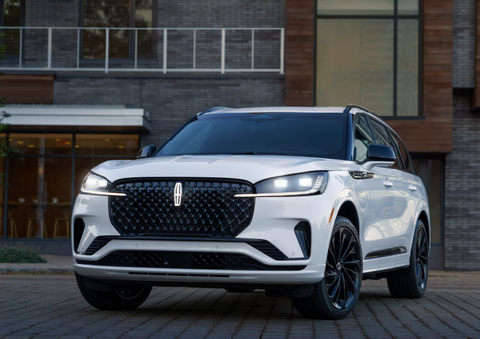 A white 2025 Lincoln Aviator® SUV is shown parked outside a modern building with gray brick and wood accents. | Korum Lincoln in Puyallup WA