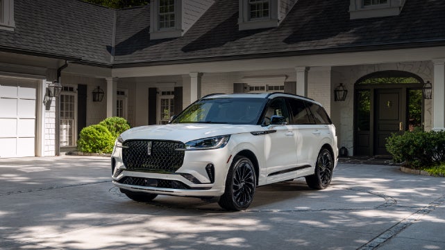 A white 2026 Lincoln Aviator® SUV is parked in the driveway of a luxury home. | Korum Lincoln in Puyallup WA
