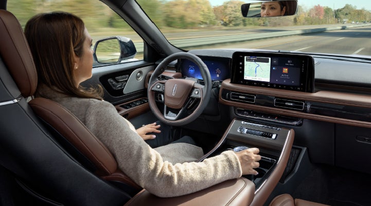 A 2027 Lincoln Aviator® SUV is being driven hands-free on a highway lined with trees. | Korum Lincoln in Puyallup WA