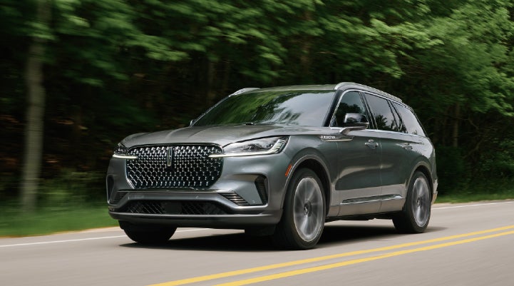 A 2027 Lincoln Aviator® SUV is being driven down a road lined with trees. | Korum Lincoln in Puyallup WA